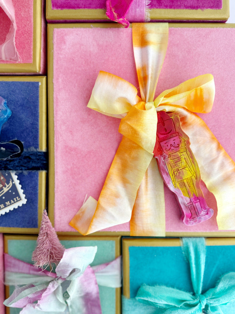 Festive gift boxes wrapped in colorful velvet ribbons and adorned with Art 2 the Extreme® Nutcracker Original Rainbow Crayons® as unique gift toppers, adding a whimsical, holiday touch