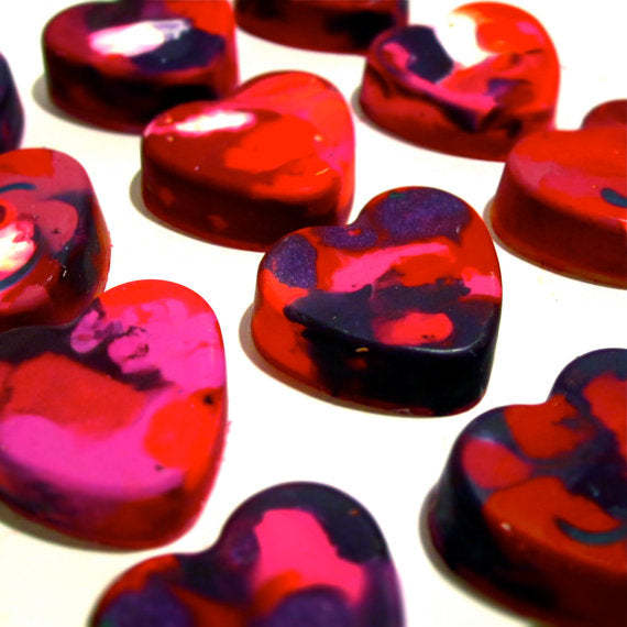 A collection of red, pink, and purple colorful heart-shaped crayons with a variety of multicolored crayon swirl patterns, arranged on a white background. These handmade crayons by Art 2 the Extreme are ideal for bulk Valentine gifts, classroom exchanges, or creative crafting fun